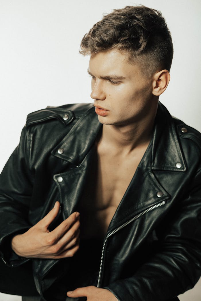 A fashionable young man posing in a black leather jacket on a white background.