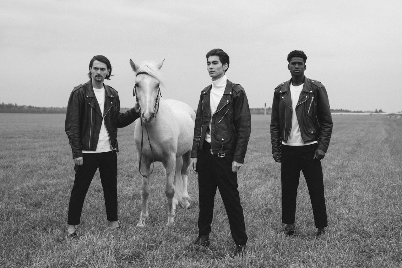 Stylish black and white photoshoot of three men in leather jackets with a white horse.