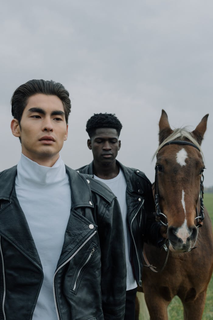 Two young men with a horse in a natural outdoor setting, wearing leather jackets.