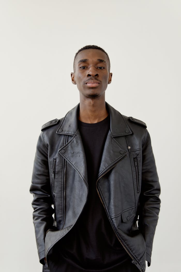 Modern portrait of a confident adult male wearing a black leather jacket against a light background.